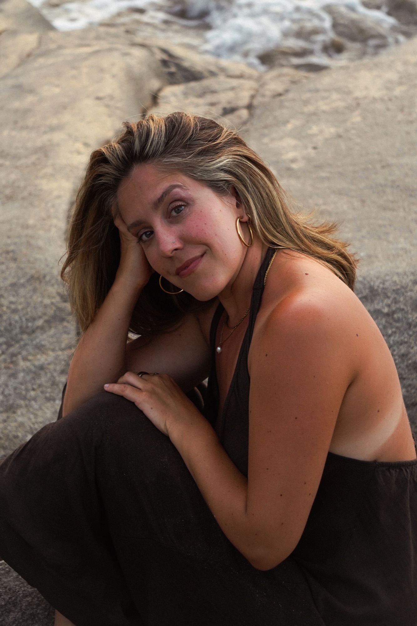 Niki seated on coastal rocks, smiling warmly at the camera